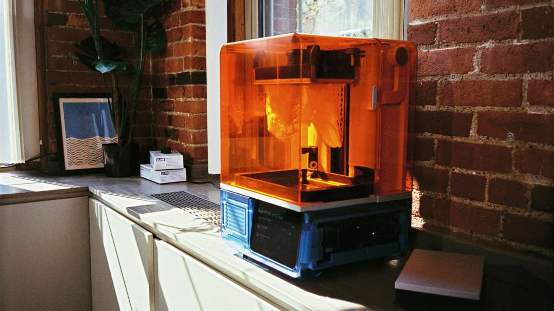 Настольный фотополимерный 3D-принтер Formlabs Form Studio 1 с оранжевым защитным колпаком на рабочем столе.