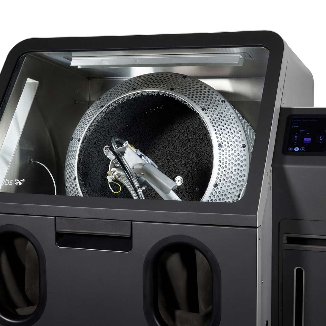 Велика барабанна корзина Formlabs Fuse Blast повністю встановлена всередині камери станції — пескоструминне сопло по центру, відбивні стінки камери з нержавіючої сталі навколо